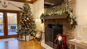Una sala de estar acogedora con un árbol de Navidad decorado, una chimenea de piedra y vistas al exterior.