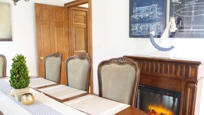 Un comedor con una mesa de madera, sillas, chimenea y un dibujo arquitectónico enmarcado en la pared.
