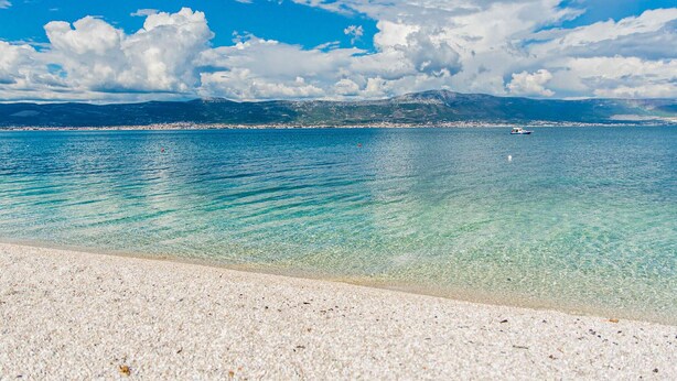 Una spiaggia con acque cristalline turchesi, una riva sabbiosa e una città all'orizzonte.