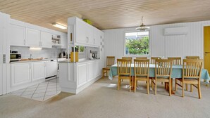 A modern kitchen with white cabinets, a dining area with wooden chairs and a table, and a large window with a view of greenery.