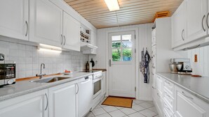 A modern kitchen with white cabinetry, a built-in oven, a coffee machine, and a window with a view of greenery.