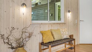 A wooden interior with a bench, a vase with branches, and two wall-mounted lights.