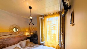 Ein ordentlich bezogenes Bett mit weißen Leinen und einem Handtuch, ein an der Wand befestigter Spiegel und ein Fenster mit gelben Vorhängen.
