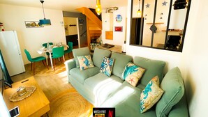 Ein gemütliches Wohnzimmer mit einem grünen Sofa, einem Essbereich mit Tisch und Stühlen sowie einer im Hintergrund sichtbaren Küche.
