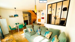 A cozy living room with a green sofa, a dining area with a table and chairs, and a kitchen visible in the background.