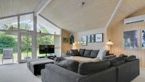 Een moderne woonkamer met een grote grijze modulaire bank, een flatscreen televisie en een eethoek met een tafel en stoelen.