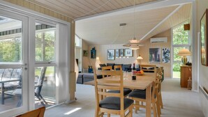 Een ruime eethoek met een houten tafel en stoelen, een bank en een groot raam met uitzicht op de omgeving.