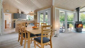 Een ruime eethoek met een houten tafel en stoelen, een keuken met houten lambrisering en een open haard met vlammen.