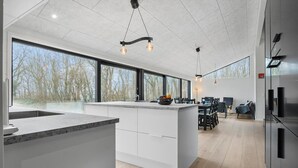 Uma cozinha moderna com uma ilha grande, amplas janelas e um espaço de refeições com cadeiras e uma mesa.