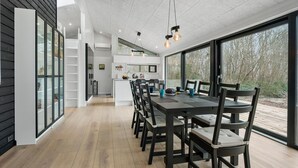 Cozinha moderna com ilha central, grandes janelas e área de jantar com uma mesa comprida e cadeiras.