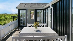 Een huisje aan zee met een balkon, een tafel met een bloemenvaas en een witte hek.