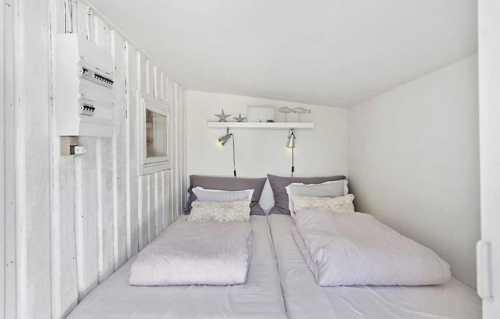 Een kleine, witte kamer met twee enkele bedden, een klein raam en een plank met decoratieve spullen.