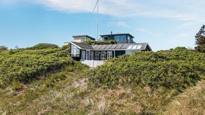 Een modern huis met een grote glazen gevel, omgeven door weelderige begroeiing.
