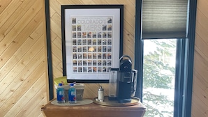 A wooden interior with a table, two stools, a framed photo of Colorado's 14ers, and a Keurig coffee maker. - Cozy Ski-In / Walk-Out @ 4 O'Clock Lodge (Breckenridge)