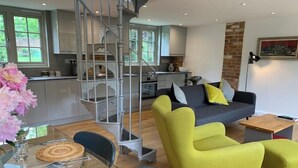 A modern living room with a sofa, chairs, and a dining table set with glassware. - Refurbished Coach House in rural setting. (Waddesdon)