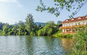 Ein Hotel am Seeufer mit einem hölzernen Balkon, umgeben von üppiger Vegetation und einer Bergkulisse.
