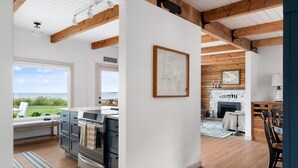 A modern kitchen with a view of the ocean, wooden beams on the ceiling, and a fireplace. - Beach Front Cottage in the Sun on Whidbey. (Greenbank)