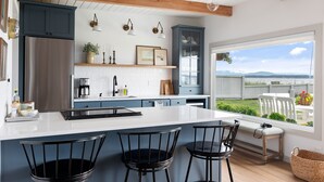 A modern kitchen with a large island, wooden beams, and a view of the outdoors. - Beach Front Cottage in the Sun on Whidbey. (Greenbank)