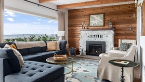 A cozy living room with a fireplace, a sofa set, and a view of the ocean. - Beach Front Cottage in the Sun on Whidbey. (Greenbank)