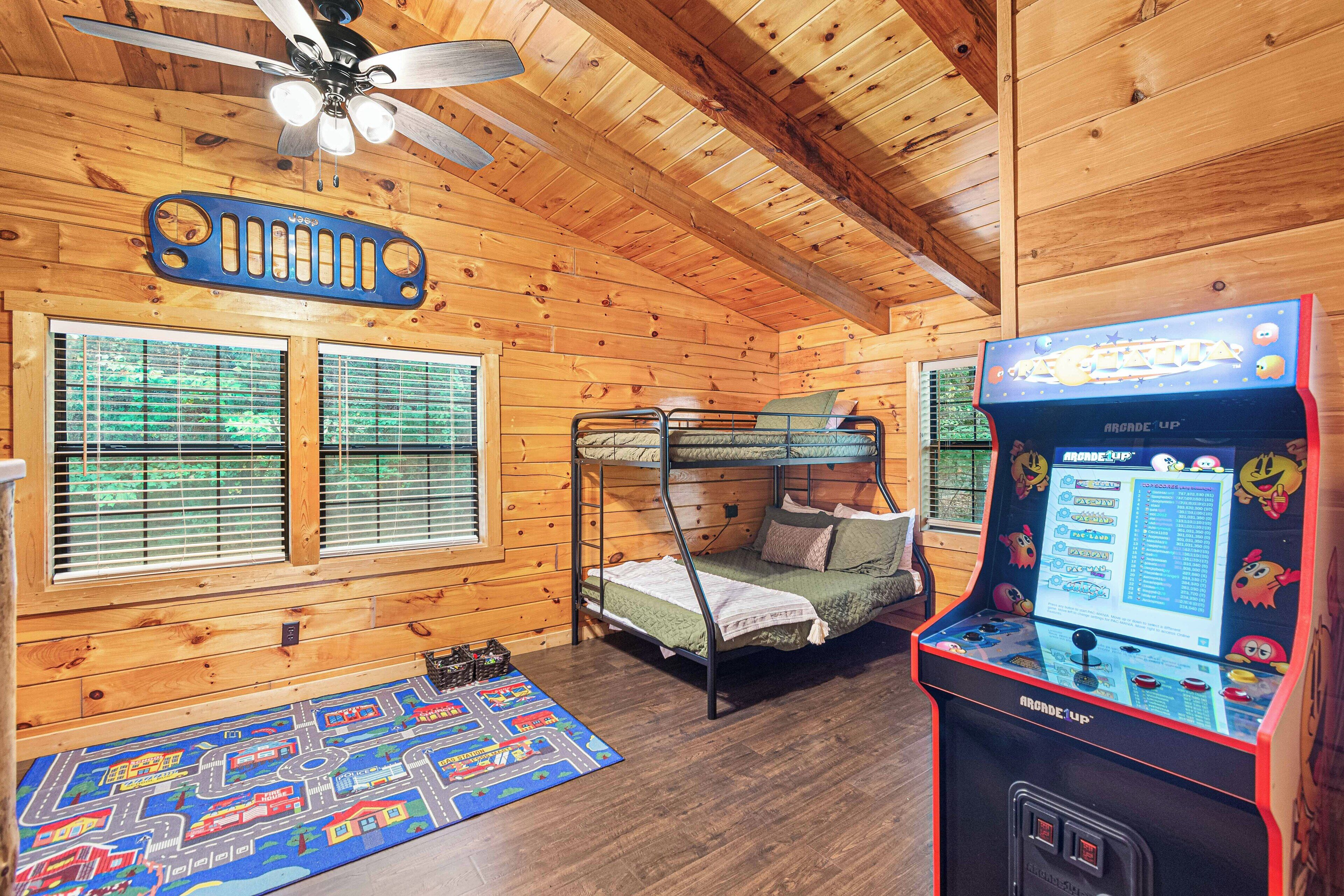Quarto com beliche, paredes de madeira, ventilador de teto e máquina de jogos.