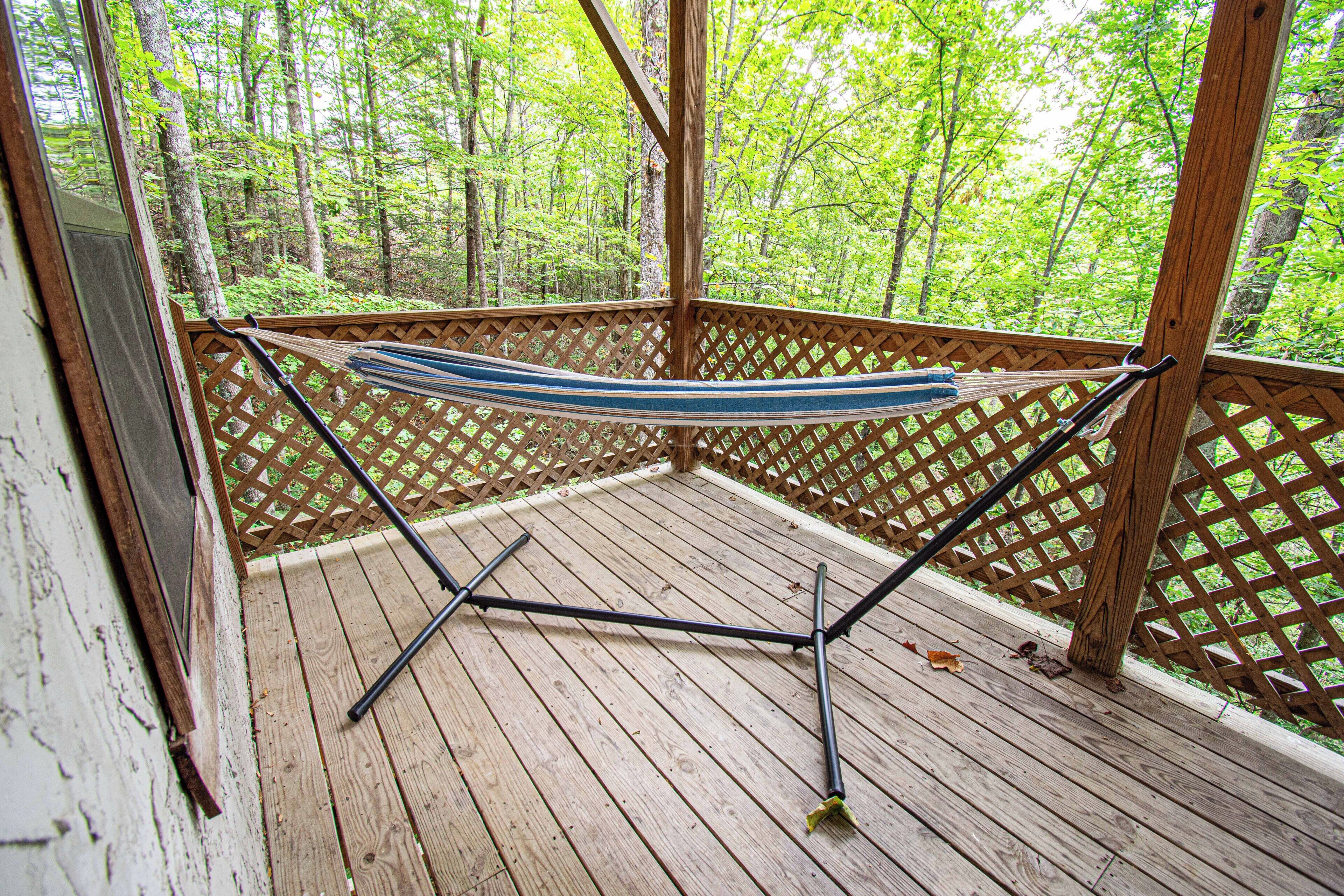 A hammock on a wooden deck with a lattice fence, surrounded by trees.