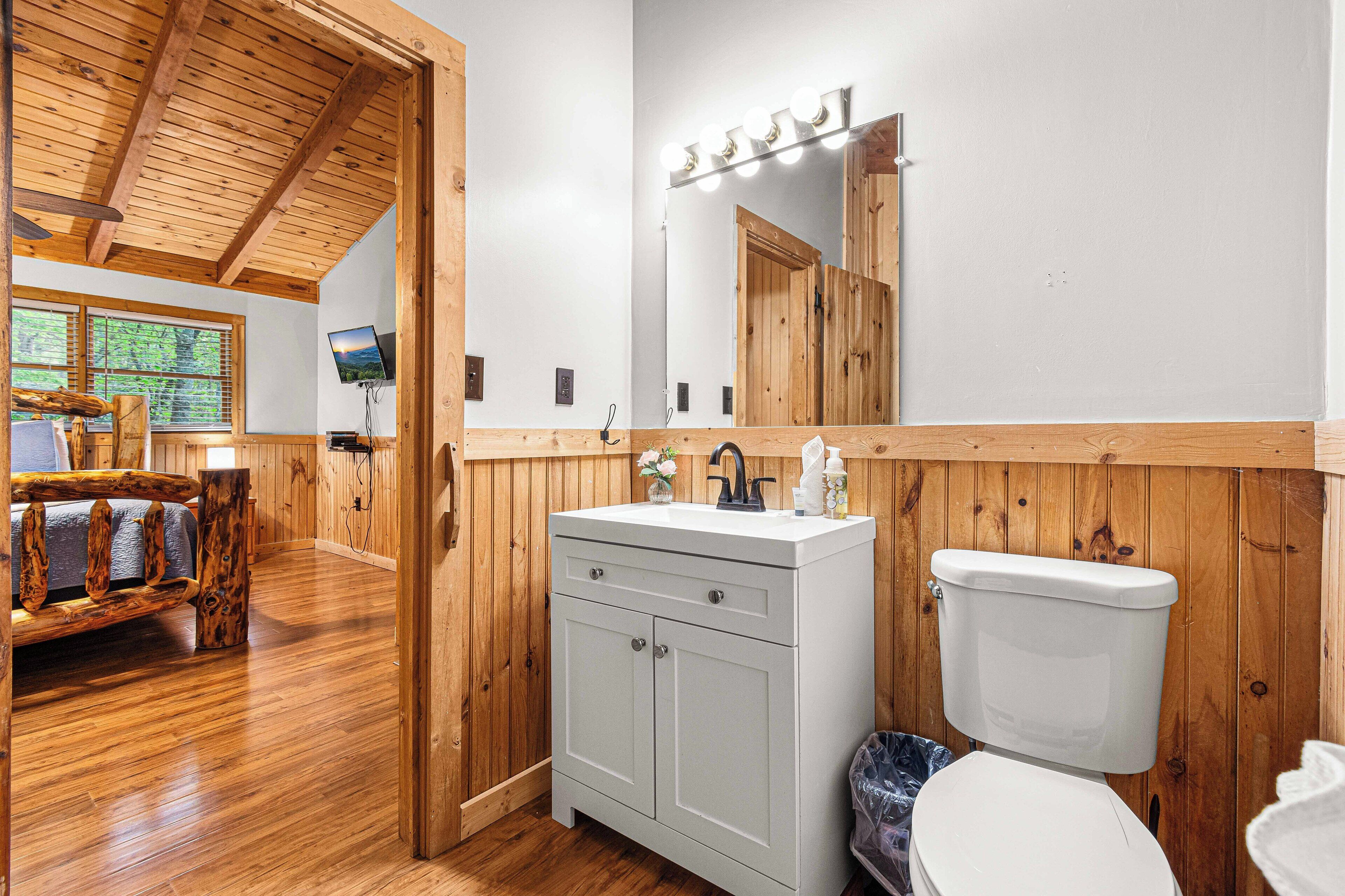 Baño de cabaña de madera con tocador de madera, inodoro y un espejo grande con iluminación.