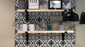 A kitchen with a patterned backsplash, a shelf with decorative items, a coffee maker, and a sink.