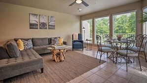 A spacious living room with a gray sofa, a coffee table with a tree stump base, a ceiling fan, and a dining area with metal chairs and a glass table.