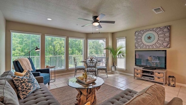 A spacious living room with a ceiling fan, large windows, a television, and a dining area.