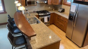 A kitchen with wooden cabinets, a stainless steel refrigerator, a microwave, a stove, and a sink.