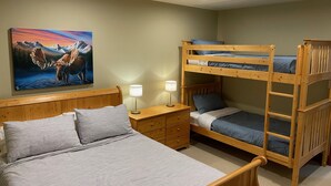 A room with a bunk bed, a single bed, a nightstand with a lamp, a wooden dresser, and a painting of moose.