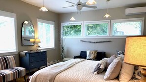 A bedroom with a bed, a dresser, a chair, a lamp, a ceiling fan, and windows with blinds.