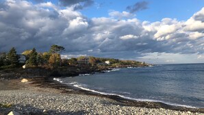 A coastal landscape with a rocky beach, a clear sky, and a few buildings in the background.