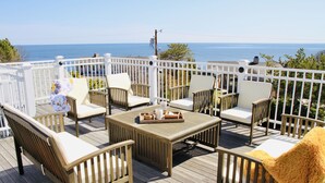 A wooden deck with outdoor furniture, including chairs and a table, overlooking a body of water.