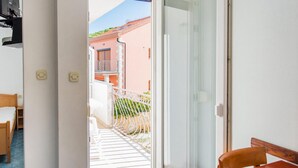 Ein schmaler Gang, der zu einem Balkon mit weißer Brüstung, einem kleinen Tisch und einem Stuhl führt.