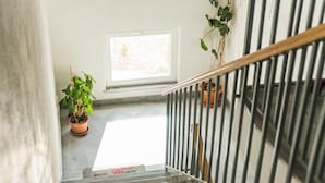 Eine Treppe mit Metallgeländer, ein Blumentopf auf der Zwischenebene und ein Fenster mit Tageslicht.