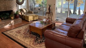 Un vaste salon doté d’une cheminée, d’un grand canapé en cuir, d’une table basse et offrant une vue sur une terrasse et un lac.