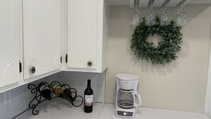 Une cuisine avec des meubles blancs, un meuble à bouteilles de vin, une machine à café et une guirlande décorative accrochée au mur.