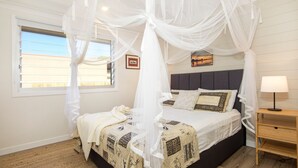 Een slaapkamer met een hemelbed, nachtkastje, lamp en raam met zonwering.