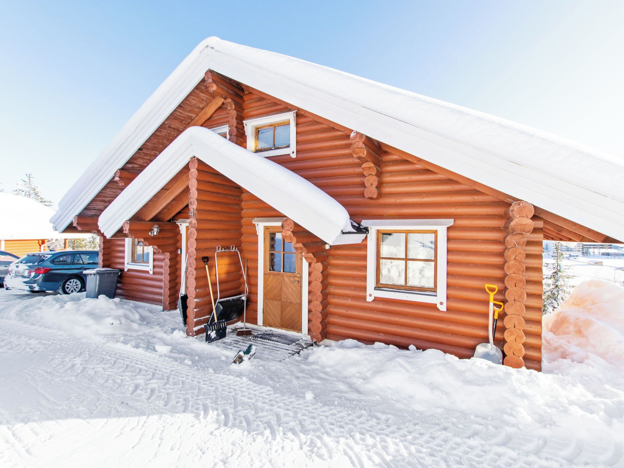 Une cabane en rondins dont le toit est recouvert de neige, avec une porte d’entrée et deux fenêtres.