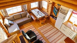 Ein gemütliches Blockhaus-Interieur mit Sofa, Esstisch, Stühlen, Fernseher und Küchenzeile.