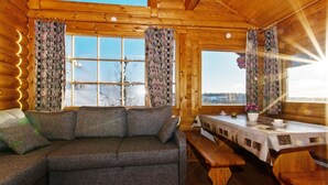 Ein gemütliches Blockhaus-Interieur mit einer Couch, einem Esstisch und großen Fenstern mit Blick auf eine verschneite Landschaft.