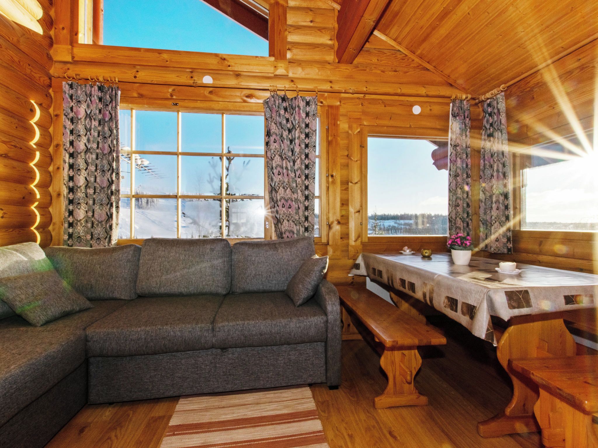 A cozy cabin interior with a sofa, wooden dining table, and large windows.