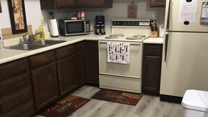 A kitchen with wooden cabinets, a white refrigerator, a stove, and a microwave. There are two wooden mats on the floor with text. - Cozy, Clean!  Pets Welcome..Close to Walking/Bike Trail (Aberdeen)