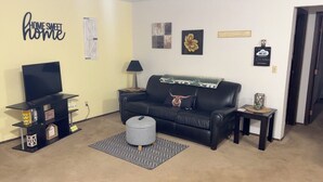 A living room with a black leather sofa, a TV, a coffee table, and a rug. There are wall decorations and a sign that says "HOME SWEET HOME". - Cozy, Clean!  Pets Welcome..Close to Walking/Bike Trail (Aberdeen)