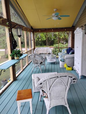 A covered porch with wicker furniture, a ceiling fan, and a view of greenery. - "Serenity Now" Beautiful Lake Front property with Pool in Sunset Beach, NC (Sunset Beach)