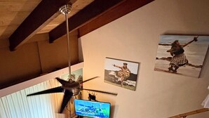 Una sala de estar con techo de madera, ventilador de techo, televisor, sofá, sillón y una escalera.