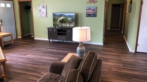Una sala de estar con piso de madera oscura, un sofá marrón, un televisor sobre un mueble negro y una lámpara.