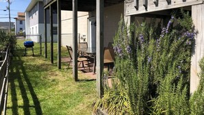 Un área de estar al aire libre cubierta con sillas y una mesa, rodeada por una terraza de madera y un jardín con flores moradas.