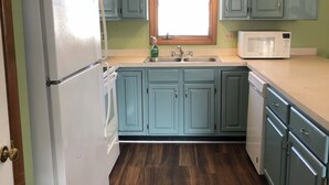 Una cocina con armarios azul claro, un refrigerador blanco, un microondas y piso de madera.
